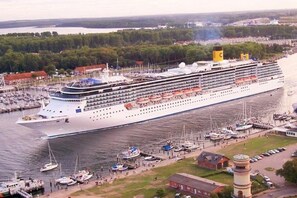 Ein großes Kreuzfahrtschiff liegt in einer Marina festgemacht, mit mehreren Decks und einem markanten Schornstein.