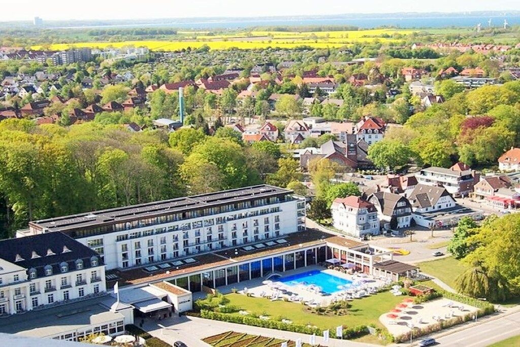 A hotel with a swimming pool, surrounded by greenery and residential buildings.