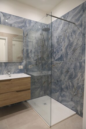 Un bagno moderno con doccia vetrata, pareti in marmo e un mobile contenitore in legno.