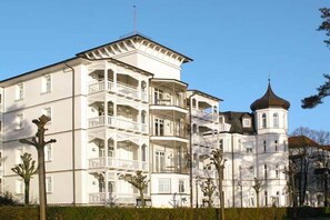 Ein mehrstöckiges Gebäude mit Balkonen, einem Eckturm und blauem Himmel.