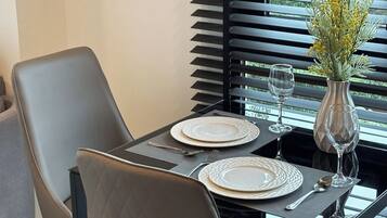 A dining table set with plates, cutlery, and a vase of flowers, positioned near a window with blinds.