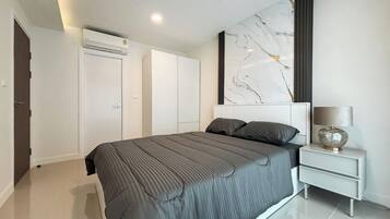 A modern bedroom with a large bed, a nightstand, a marble artwork, and built-in wardrobes.