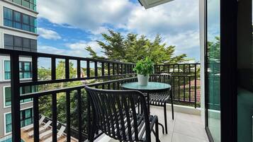 A balcony with a table and chairs, a potted plant, and a view of a swimming pool and buildings.