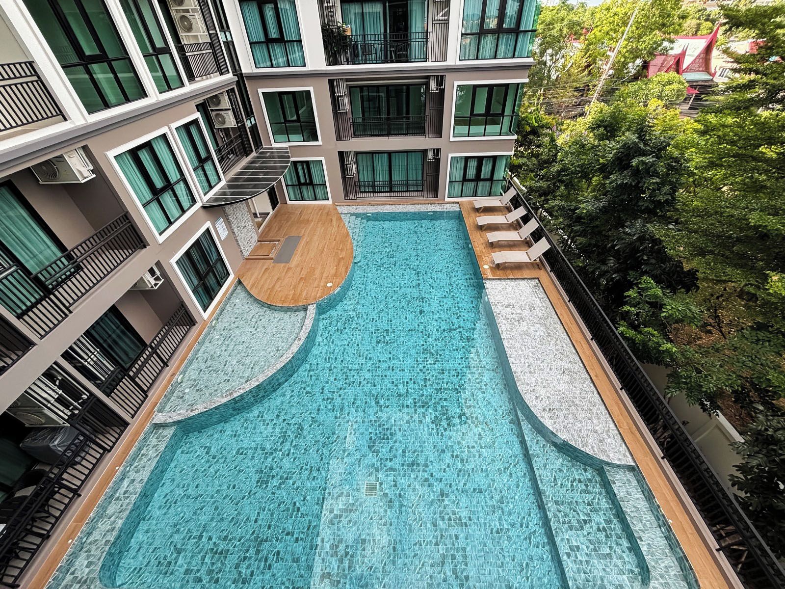 A modern building with a central swimming pool, multiple balconies, and surrounding greenery.