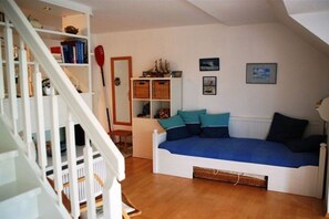 Una habitació amb una escala blanca, un llit blanc amb roba de llit blava, una biblioteca i una taula petita amb una pala vermella.
