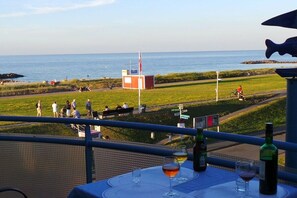 A balcony with a table set for two, overlooking a beach and a grassy area with people. - Holiday apartment with 1 bedroom (Schönberger Strand)