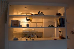 A kitchen with white cabinets, a countertop, and shelves with various items including a bird figurine, a wine glass, and books. - Holiday apartment with 1 bedroom (Schönberger Strand)