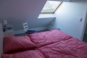 A bedroom with a skylight, a bed with pink bedding, a chair, and a nightstand with a lamp. - Holiday apartment with 1 bedroom (Schönberger Strand)