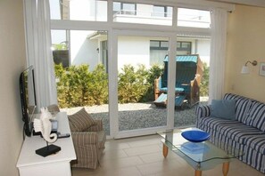 Ein Wohnzimmer mit einer Couch, einem Glastisch und einem Fernseher auf einer weißen Kommode.