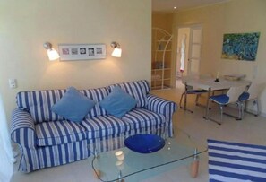Ein Wohnzimmer mit einem gestreiften Sofa, einem Glastisch und einem Essbereich mit Tisch und Stühlen.