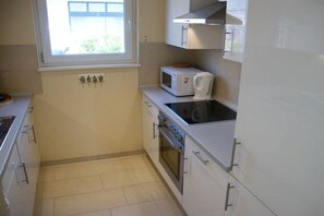 Eine kompakte Küche mit weißen Schränken, einer Mikrowelle, einem Backofen und einem Fenster mit Blick auf Grünflächen.