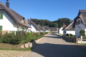Eine Reihe traditioneller Häuser mit Strohdächern, eine gepflasterte Straße und eine Steinmauer an einer Seite.