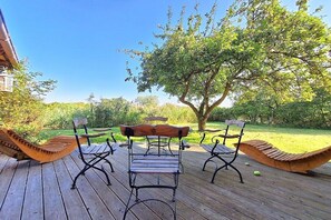A wooden deck with a bench and a table, surrounded by greenery and a tree. - Holiday home in Sterup with swimming pool (Sterup)