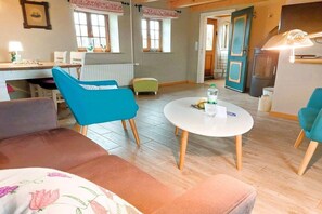 A living room with a round white table, blue chairs, a brown sofa, and a green ottoman. - Holiday home with 2 bedrooms (Steinbergkirche)