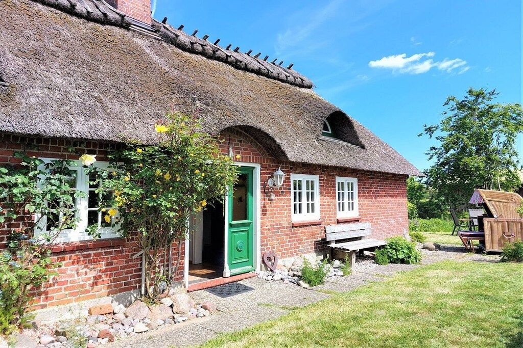 A traditional brick house with a thatched roof, a green door, and a small garden area with a bench and outdoor furniture.