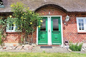 A brick house with a green door, a small window, and a thatched roof. - Holiday home with 2 bedrooms (Steinbergkirche)