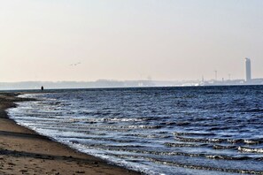 A beach with waves, a distant person, and a cityscape with buildings and cranes. - Baltic Sea residence Barendorf (Barendorf\/Dassow)