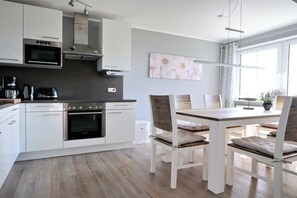 A modern kitchen with white cabinetry, a built-in oven, and a dining area with a wooden table and chairs. - Baltic Sea residence Barendorf (Barendorf\/Dassow)