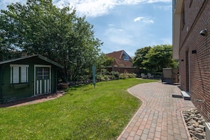 A brick pathway leading to a green shed and a house with a sloped roof. - Strandkieker Achtern (St. Peter-Ording)