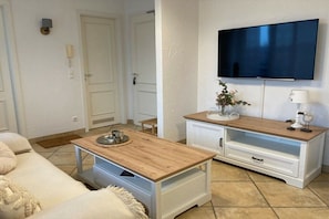 A living room with a sofa, wooden coffee table, white cabinet, and a flat-screen TV mounted on the wall. - Apartment building Miramare (Ostseebad Kühlungsborn)