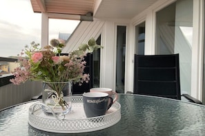 Een glazen tafel met een dienblad, een vaas met bloemen en twee mokken erop.