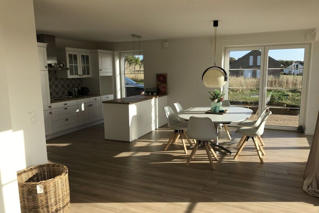 Une cuisine moderne avec des meubles blancs, un coin repas doté d’une table ronde et de chaises, et une grande fenêtre offrant une vue sur l’extérieur.