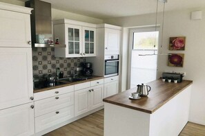 A modern kitchen with white cabinetry, a wooden countertop, and a window with blinds. - Holiday home with 3 bedrooms (Hohwacht (Ostsee))