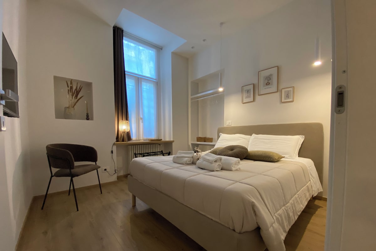 Un dormitorio moderno con una cama grande, una silla, un ventanal con cortinas y un radiador.