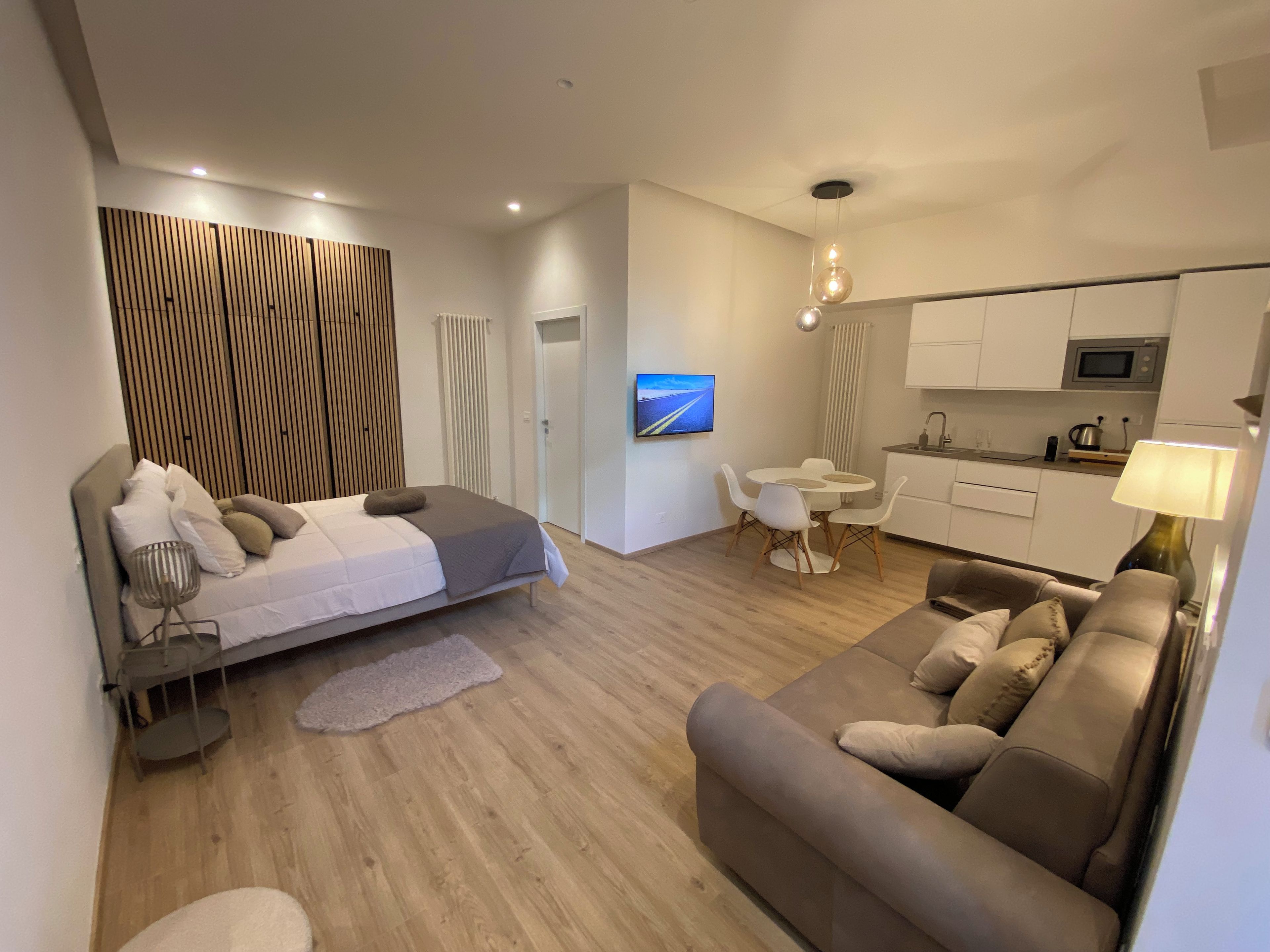 A modern, well-lit bedroom with a bed, bedside table, and a TV mounted on the wall.