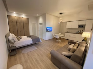 Un dormitorio moderno y bien iluminado con cama, mesita de noche y televisor montado en la pared.
