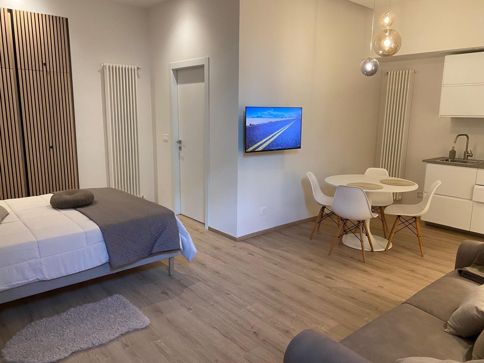 Une chambre d’hôtel moderne comprenant un lit, un coin repas avec une table et des chaises, un téléviseur fixé au mur et une kitchenette.