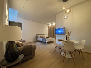 Una habitación de hotel moderna con cama, zona de comedor, televisión y lámpara.