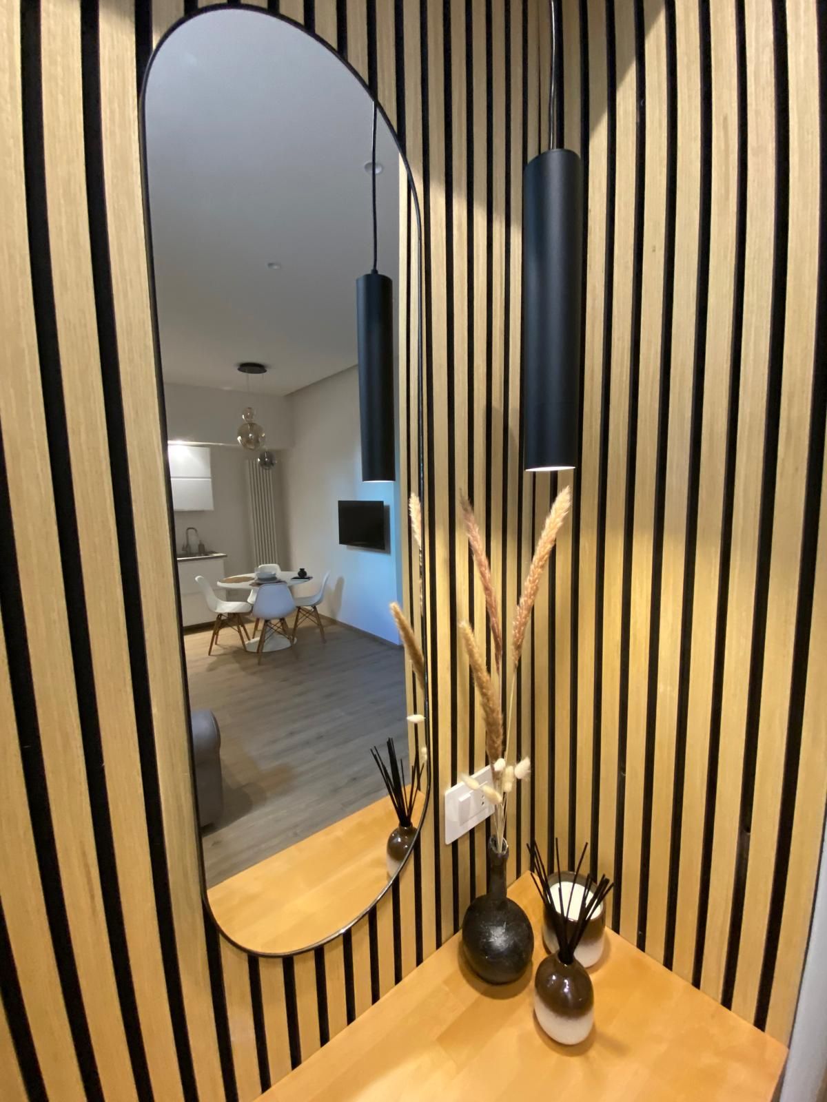 A modern interior with a wooden slatted wall, a round mirror, and a small table with decorative items.