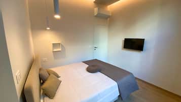 Un dormitorio con cama, mesita de noche, televisor en la pared y una puerta.