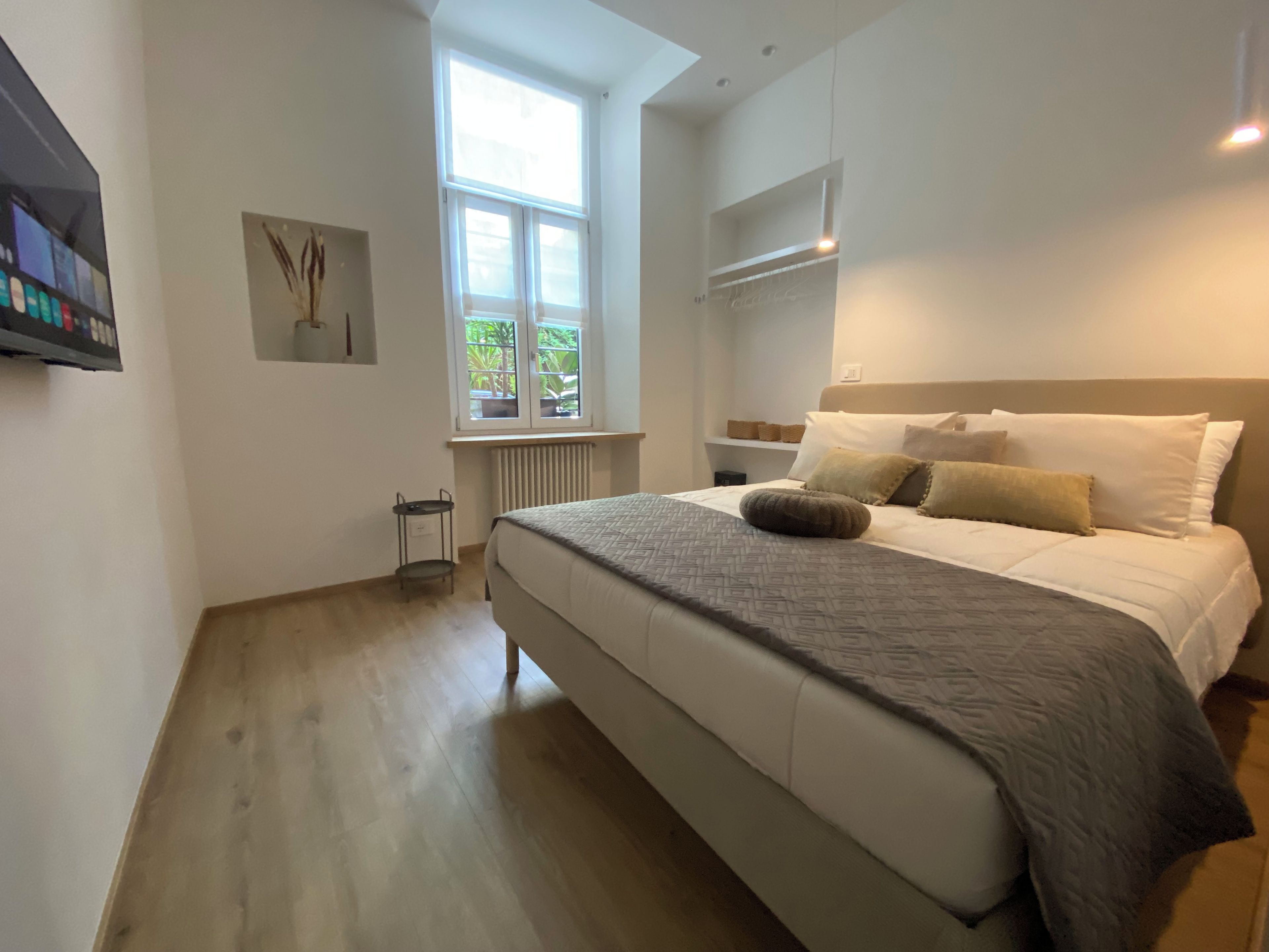 Un dormitorio con una cama grande, una ventana con vistas a zonas verdes, un radiador y una estantería de pared.