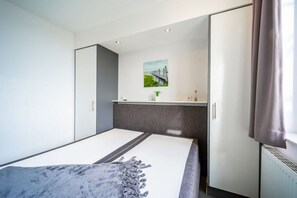 Ein modernes Schlafzimmer mit einem Bett, einer kleinen Küchenzeile und einem Fenster mit Vorhängen.