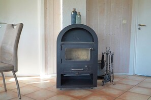 Ein Zimmer mit einem schwarzen Kaminofen, einem Sessel und einer Tür.