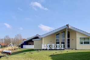 Ein eingeschossiges Gebäude mit geneigtem Dach, einem großen Fenster und einem weißen Zaun.
