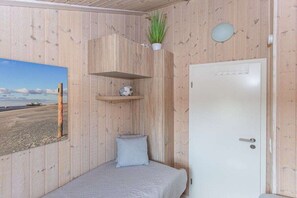 Ein Zimmer mit Holzwänden, einem Bett mit Kissen, einem Regal mit einer Pflanze und einer Tür.
