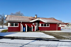 A red building with a sloped roof, a satellite dish, and a blue trash bin in front. - Holiday home with 1 bedroom (Otterndorf)