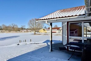 A covered outdoor area with a snow-covered deck, a table, and a building with a tiled roof in the background. - Holiday home with 1 bedroom (Otterndorf)