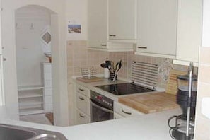 Una cocina con armarios blancos, estufa, horno y encimera con hervidor.
