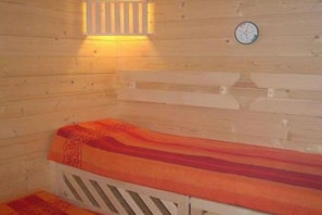 A wooden cabin interior with a bed, a wall-mounted clock, and a window with blinds. - A holiday with flair - Sternberg (Sternberg)