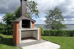An outdoor brick pizza oven with a chimney, set against a backdrop of a lake and trees. - A holiday with flair - Sternberg (Sternberg)