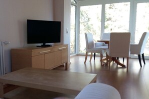 Ein modernes Wohnzimmer mit Flachbildfernseher, Holzmöbeln und großen Fenstern.
