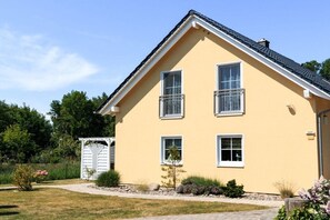 Ein zweistöckiges Haus mit gelbem Anstrich, einem geneigten Dach und einem kleinen Garten mit einem weißen Tor.