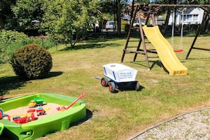 Ein Spielplatz mit einer gelben Rutsche, einer Schaukel und einem grünen Sandkasten.