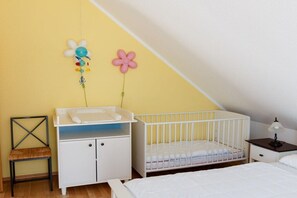Ein Zimmer mit einem Babybett, einem kleinen Schreibtisch und einem Stuhl.