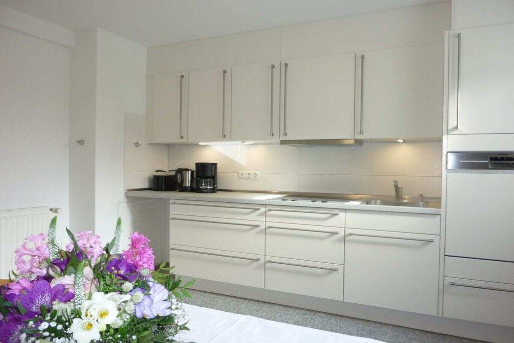 Una cocina moderna con armarios blancos, un refrigerador de acero inoxidable y una cafetera en la encimera.