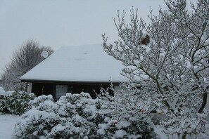 Um edifício com telhado coberto de neve e árvores ao redor carregadas de neve.